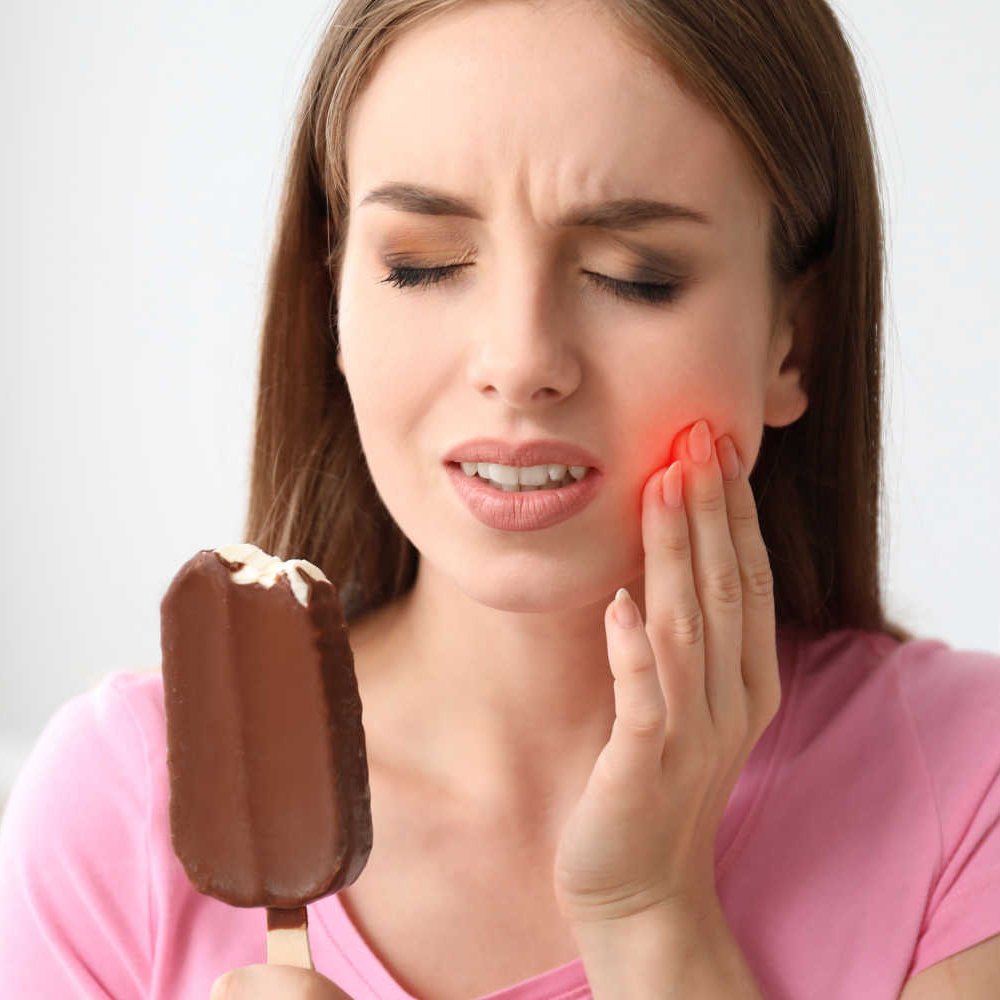 Woman wincing in pain from cold food due to tooth sensitivity